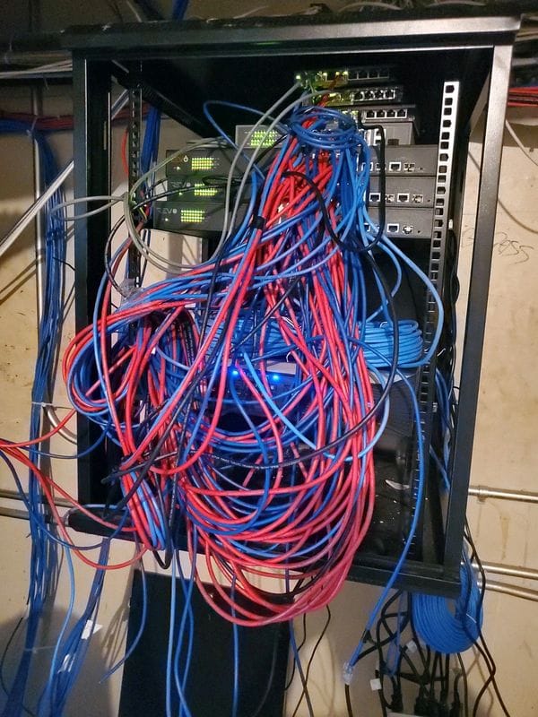 Open server rack overloaded with a tangled mass of loose red and blue network cables