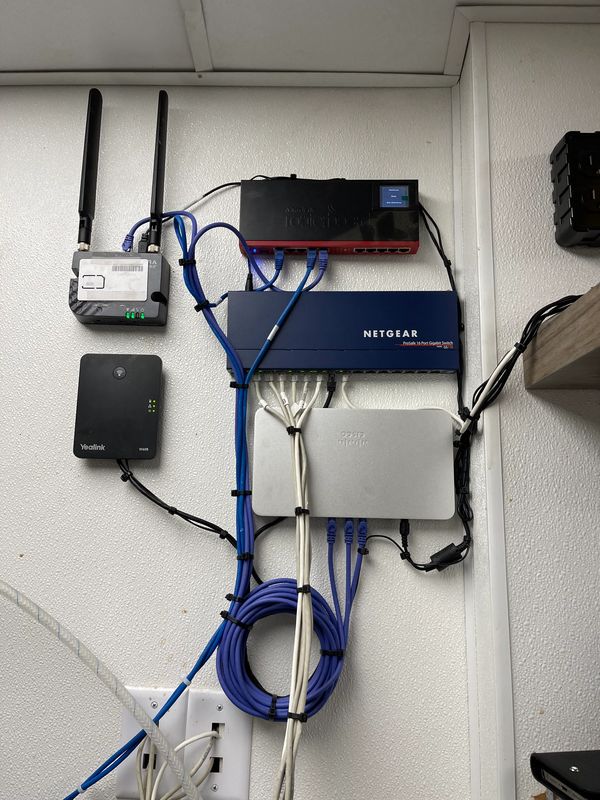 The same hardware wall-mounted: switch, modem and VoIP adapter secured with cables clipped and coiled