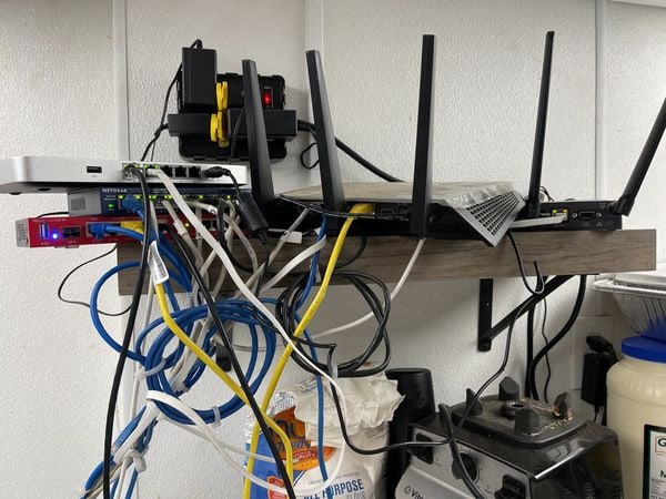 Routers and a switch balanced on a wooden shelf with cables hanging loose beneath it