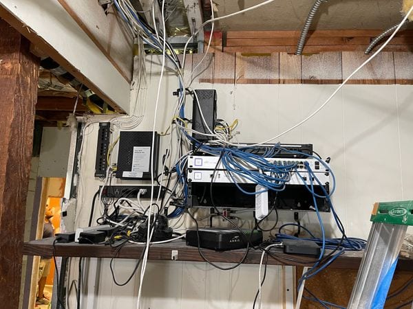 Network gear on an unfinished basement shelf with cables draped across exposed framing