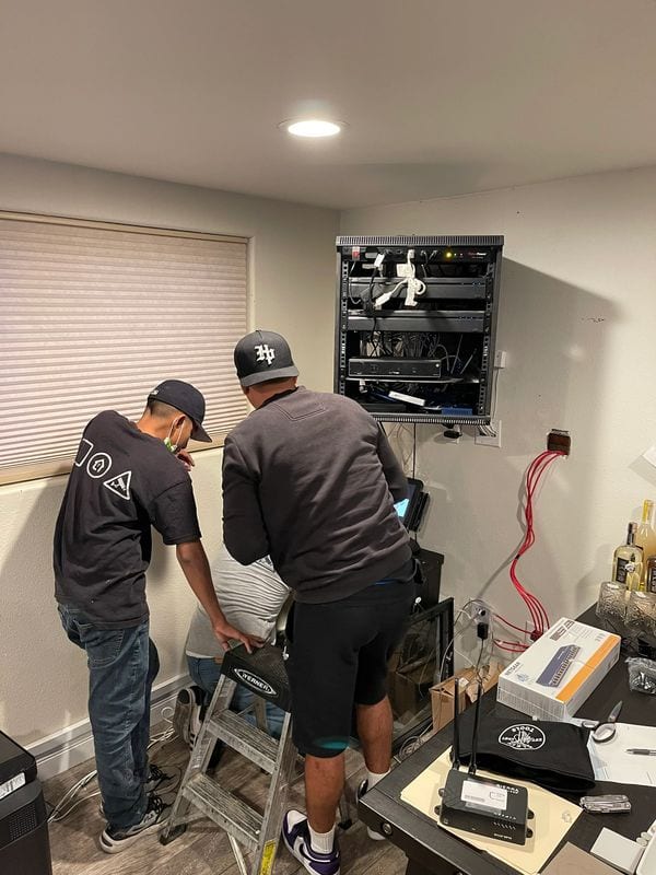 Two Payco technicians terminating cable at a wall-mounted rack during an on-site install