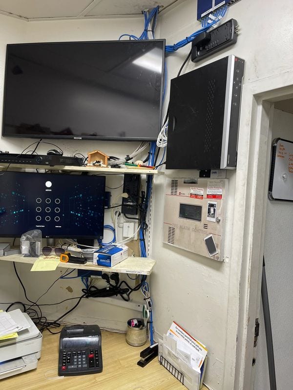 The same back office after cleanup: displays mounted, recorder shelved, cable runs bundled to the wall