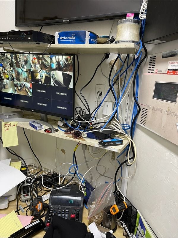 Back-office camera monitor and shelving with power and network cables running loose down the wall